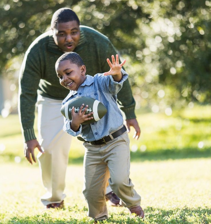 Joyful Black father smiling and playing with his child outdoors in golden sunlight